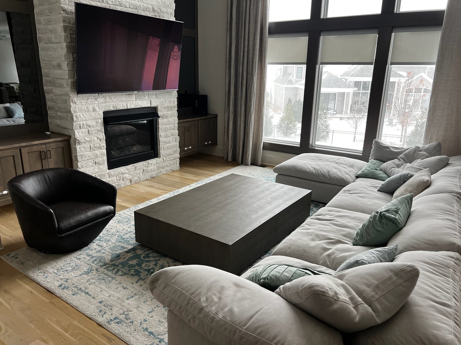 A family room with a stone fireplace and TV beside a tall window wall, every shade lowered to the same line across the panes