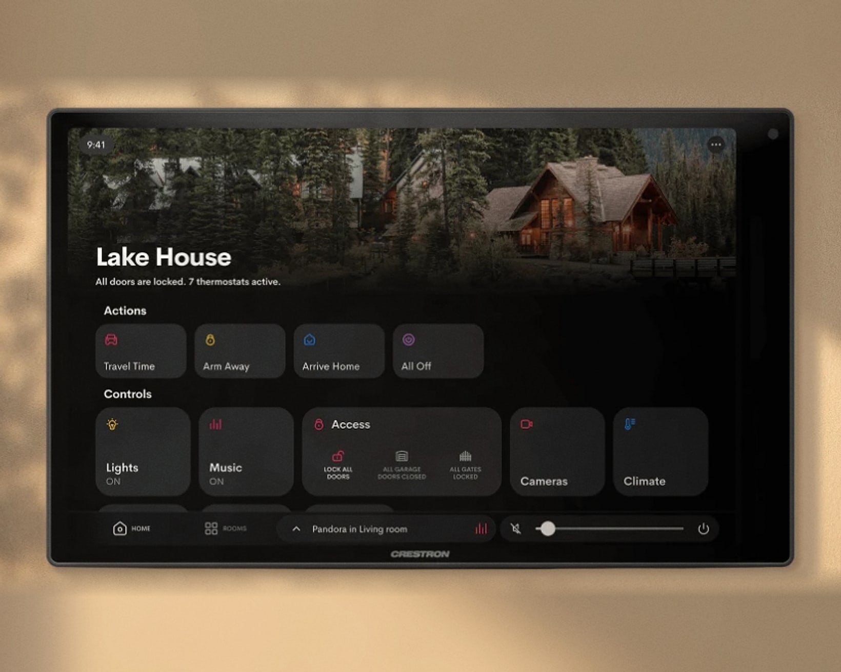 A Crestron touch panel on a plaster wall, showing the Crestron Home screen for a lake house: actions, lights, music, access, cameras and climate.