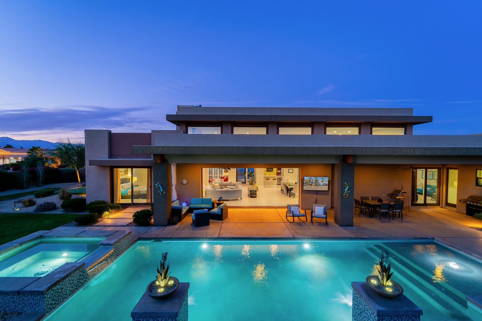 A modern home at dusk, the pool and patio lit.